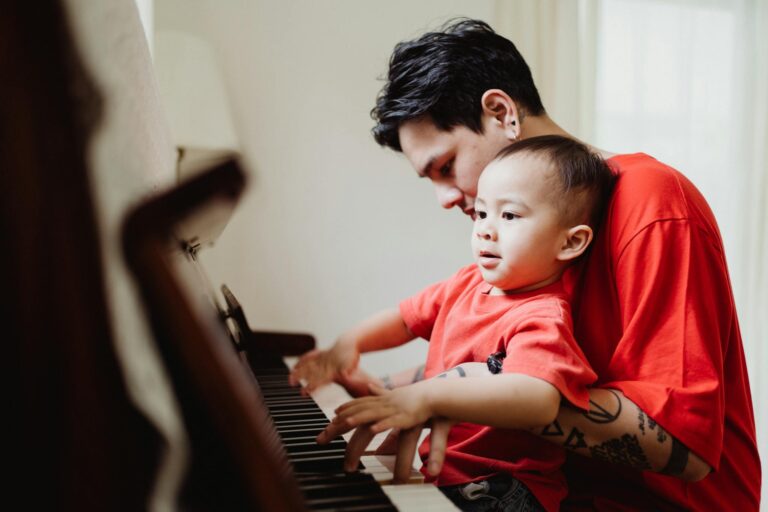 A father and son bond over playing the piano together in a bright living room.