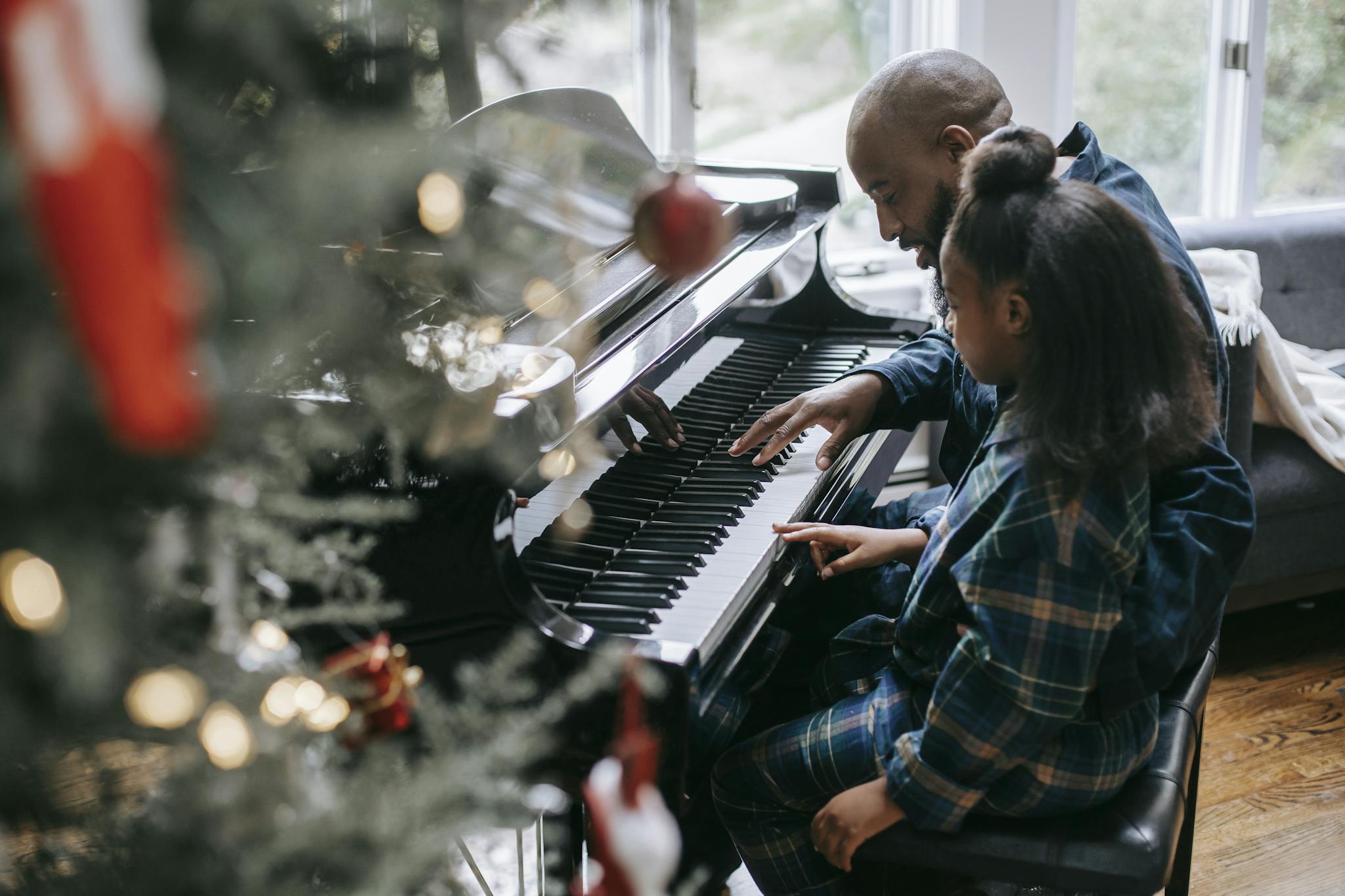 A touching scene of a father and daughter playing piano together by the Christmas tree.